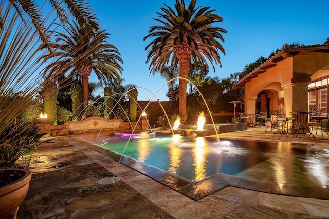 pool at dusk featuring pool water feature and a patio