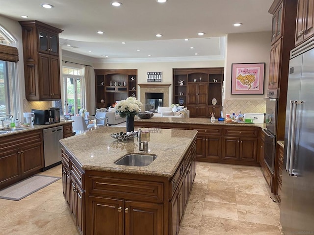 kitchen with light stone countertops, an island with sink, appliances with stainless steel finishes, and ornamental molding