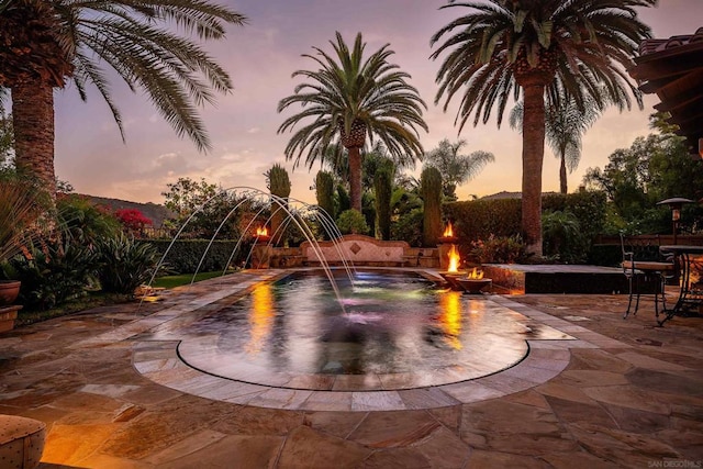 pool at dusk with a mountain view, a patio, and an outdoor fire pit