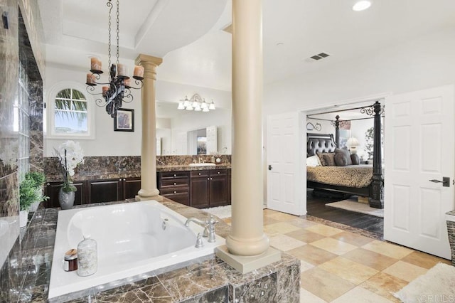 bathroom featuring vanity, decorative columns, and tiled tub