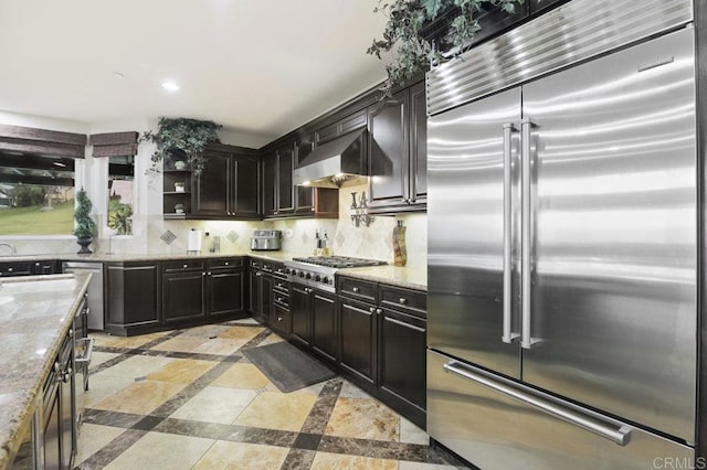 kitchen featuring light stone countertops, backsplash, stainless steel appliances, and wall chimney exhaust hood