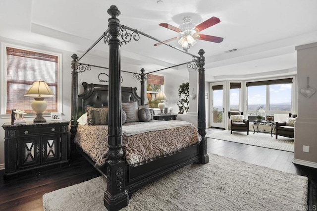 bedroom featuring dark wood-type flooring, ceiling fan, access to exterior, and a raised ceiling