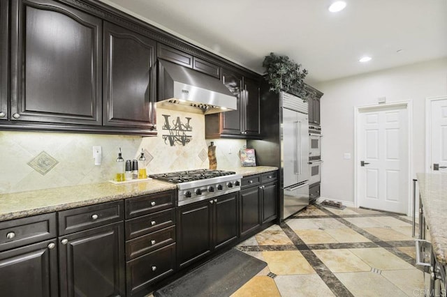 kitchen with tasteful backsplash, wall chimney range hood, light stone counters, and stainless steel gas cooktop