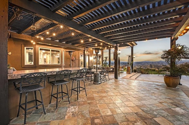 patio terrace at dusk featuring a pergola and exterior bar