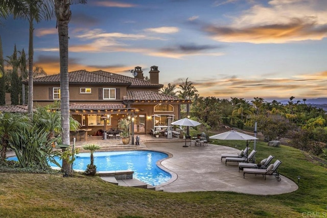 pool at dusk with a patio and a lawn