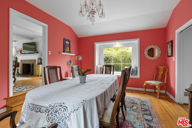 dining area with lofted ceiling, a notable chandelier, a fireplace, and light hardwood / wood-style floors