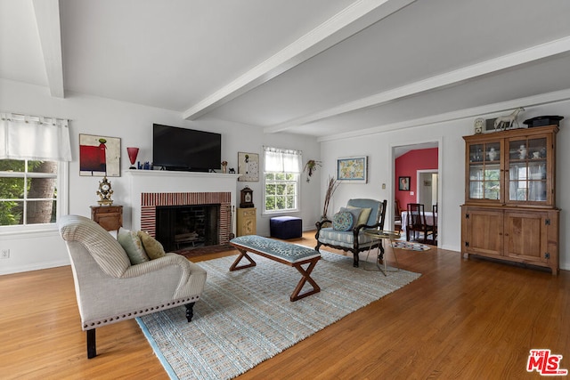 living room featuring beam ceiling, a brick fireplace, and hardwood / wood-style flooring