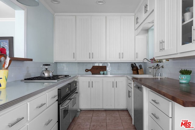 kitchen featuring wood counters, stainless steel appliances, light tile patterned floors, and white cabinets