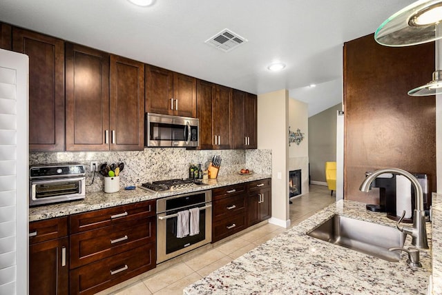 kitchen with sink, light tile patterned floors, appliances with stainless steel finishes, tasteful backsplash, and light stone countertops