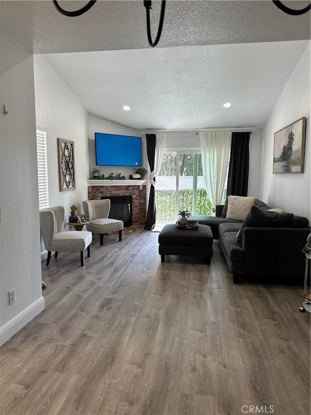 living room featuring hardwood / wood-style floors, a fireplace, a textured ceiling, and vaulted ceiling