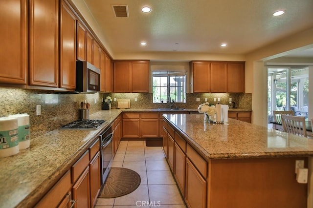 kitchen with appliances with stainless steel finishes, tasteful backsplash, sink, light tile patterned floors, and light stone counters