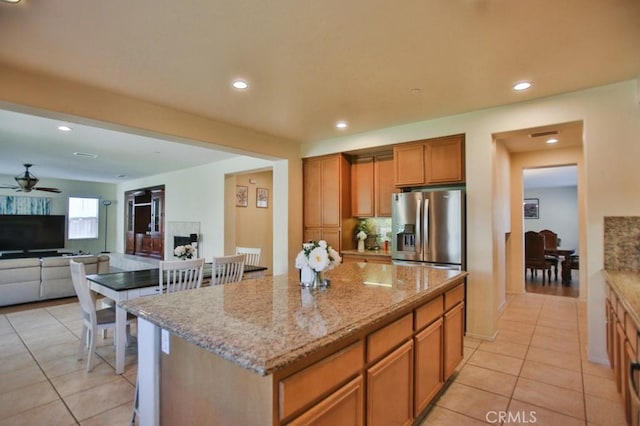 kitchen featuring a kitchen island, backsplash, ceiling fan, light stone counters, and stainless steel refrigerator with ice dispenser