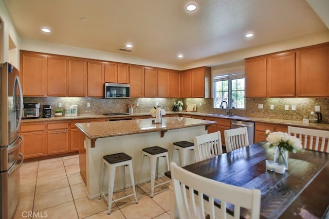 kitchen with a kitchen breakfast bar, decorative backsplash, a center island, light stone counters, and stainless steel appliances