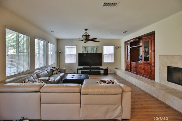 living room with a fireplace, ceiling fan, and light wood-type flooring