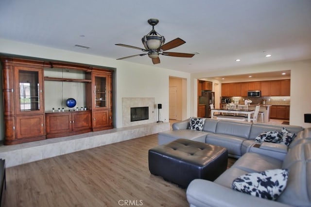 living room featuring a premium fireplace, ceiling fan, and light wood-type flooring