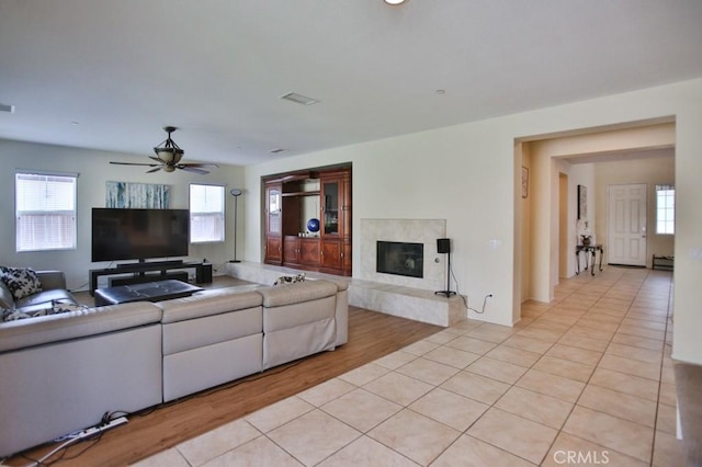 living room featuring ceiling fan, a premium fireplace, and light tile patterned floors