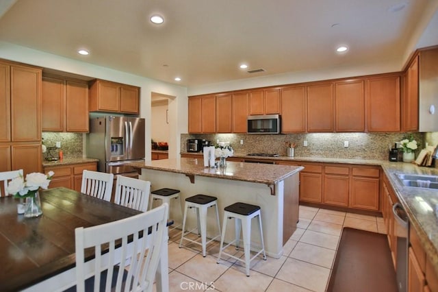 kitchen featuring light tile patterned floors, appliances with stainless steel finishes, a kitchen breakfast bar, light stone countertops, and a kitchen island