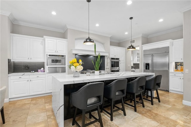 kitchen with light stone counters, decorative light fixtures, a large island with sink, stainless steel appliances, and white cabinets