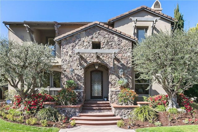 view of front of home featuring a tiled roof, a balcony, stone siding, and stucco siding