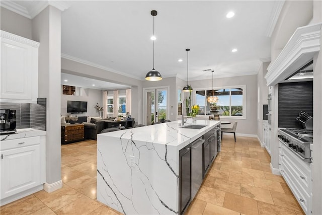 kitchen with stainless steel gas stovetop, an island with sink, sink, white cabinets, and hanging light fixtures