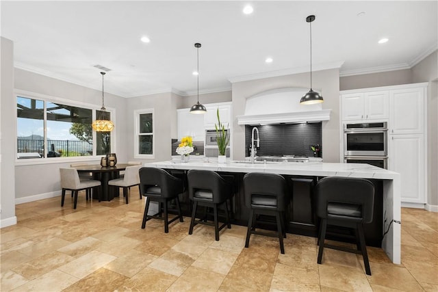 kitchen with a spacious island, decorative light fixtures, double oven, light stone countertops, and white cabinets