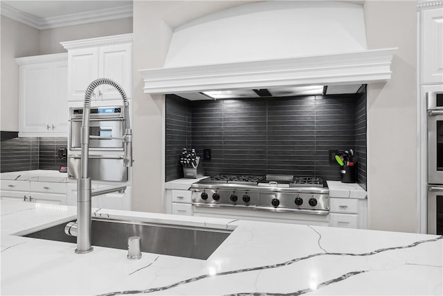 kitchen featuring premium range hood, stove, light stone counters, tasteful backsplash, and white cabinets