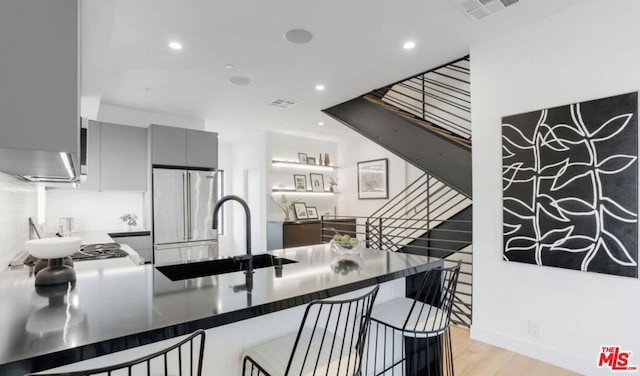 kitchen with sink, gray cabinetry, high end refrigerator, kitchen peninsula, and light hardwood / wood-style flooring