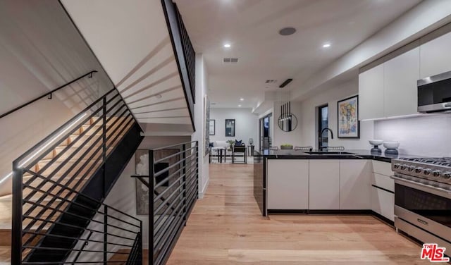 kitchen featuring white cabinetry, sink, kitchen peninsula, stainless steel appliances, and light hardwood / wood-style flooring