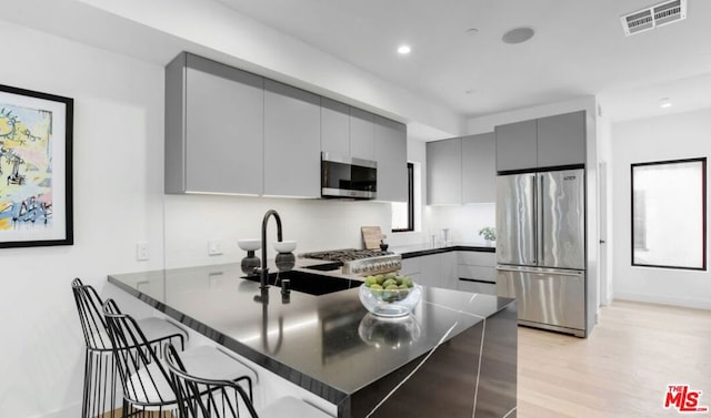 kitchen featuring a kitchen bar, gray cabinetry, light hardwood / wood-style flooring, appliances with stainless steel finishes, and kitchen peninsula