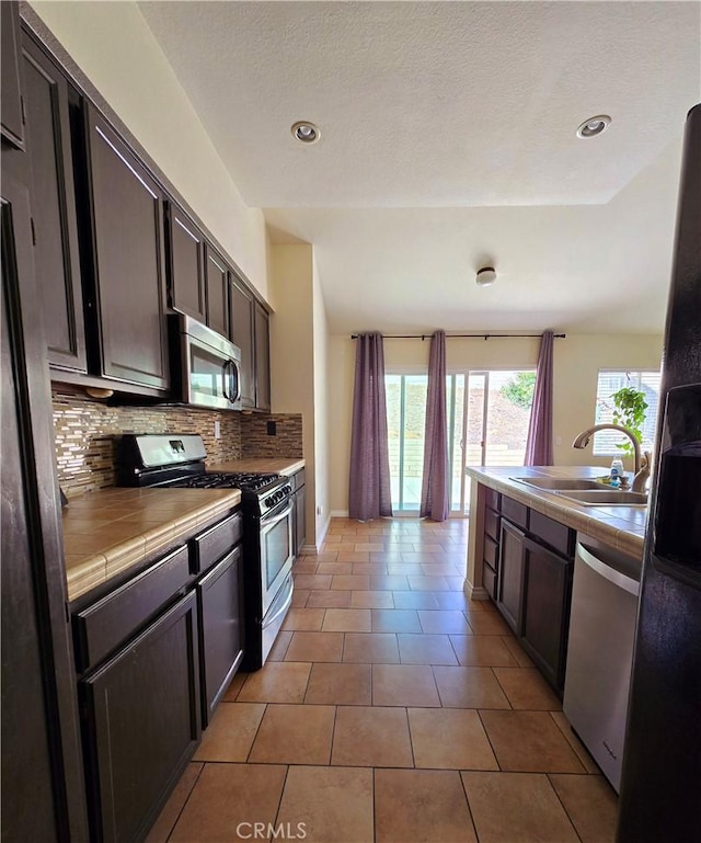 kitchen featuring dark brown cabinetry, stainless steel appliances, tile countertops, and a sink