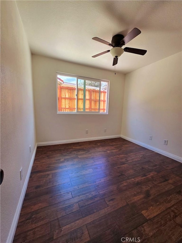 unfurnished room featuring dark wood-style flooring, a ceiling fan, and baseboards