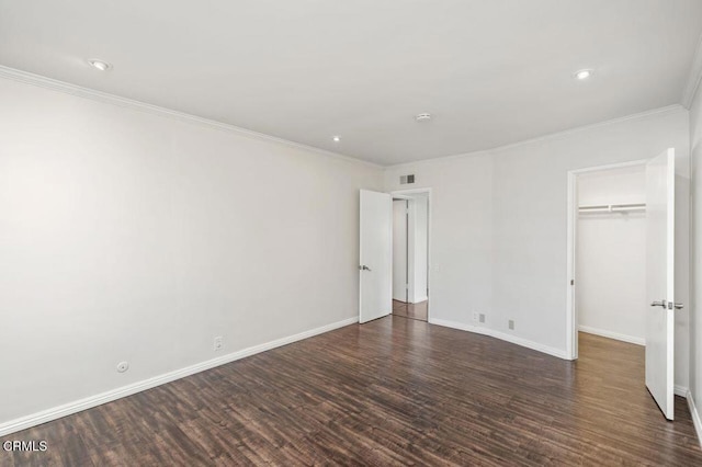 unfurnished bedroom featuring crown molding, a walk in closet, dark wood-type flooring, and a closet