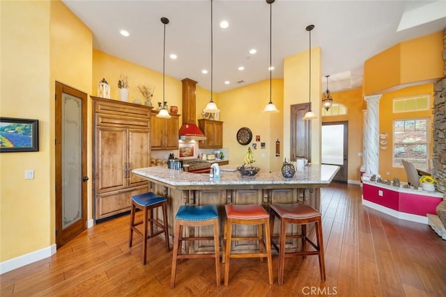 kitchen featuring pendant lighting, decorative columns, a kitchen breakfast bar, paneled built in refrigerator, and light stone countertops