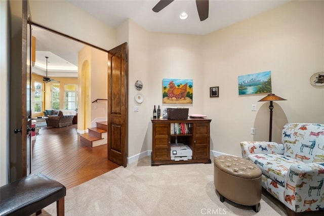 sitting room with a raised ceiling, carpet flooring, and ceiling fan