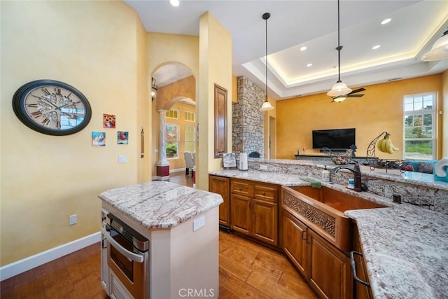 kitchen featuring light stone counters, a raised ceiling, sink, and oven