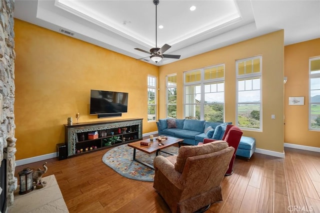 living room featuring ceiling fan, a fireplace, a tray ceiling, and hardwood / wood-style floors