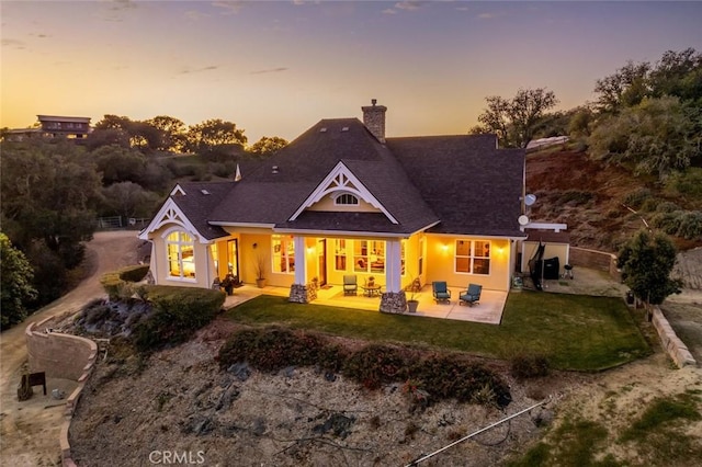 back house at dusk featuring a yard and a patio