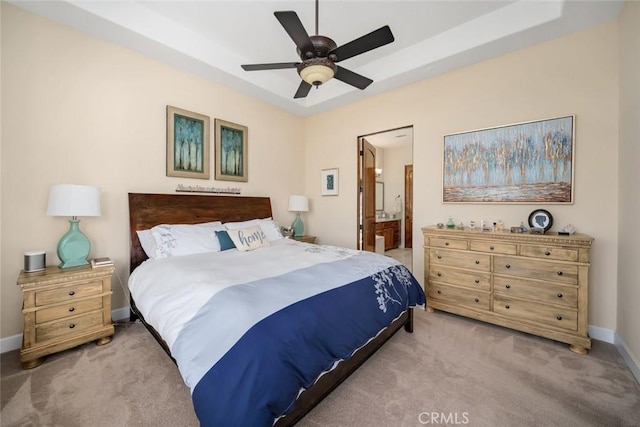 bedroom featuring ceiling fan, ensuite bath, a tray ceiling, and carpet flooring