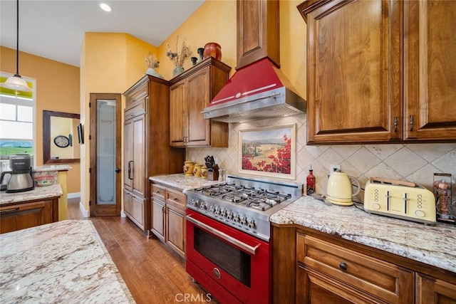 kitchen featuring light stone counters, premium appliances, extractor fan, light hardwood / wood-style floors, and decorative light fixtures