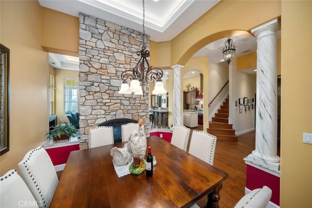 dining area with a tray ceiling, wood-type flooring, a chandelier, and ornate columns