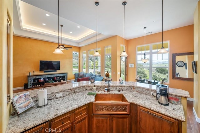 kitchen with light stone countertops, a raised ceiling, hanging light fixtures, and a wealth of natural light