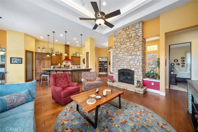 living room featuring a stone fireplace, dark hardwood / wood-style floors, a raised ceiling, and ceiling fan