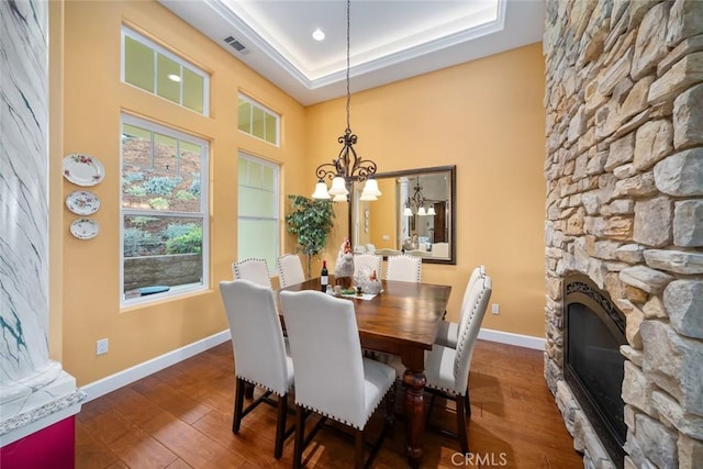 dining area with dark hardwood / wood-style flooring, a fireplace, a raised ceiling, and a chandelier