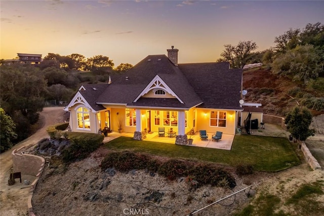 back house at dusk with a patio area and a lawn