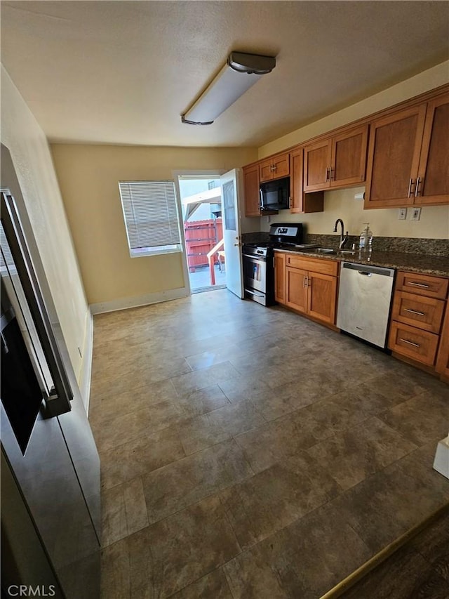kitchen with brown cabinetry, dark countertops, a sink, baseboards, and stainless steel appliances