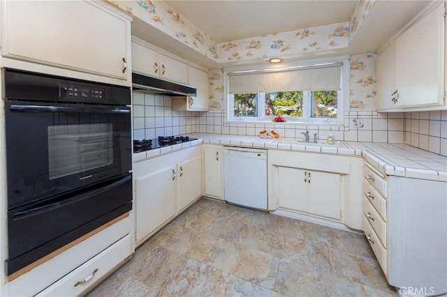 kitchen with gas stovetop, white cabinetry, tile counters, white dishwasher, and oven