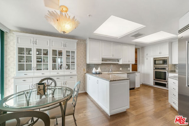 kitchen featuring a skylight, sink, white cabinets, light stone counters, and stainless steel appliances