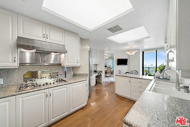 kitchen featuring sink, a skylight, light hardwood / wood-style floors, white cabinets, and stainless steel gas stovetop