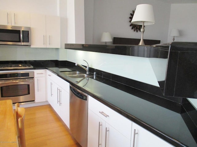 kitchen featuring appliances with stainless steel finishes, sink, white cabinets, and light wood-type flooring