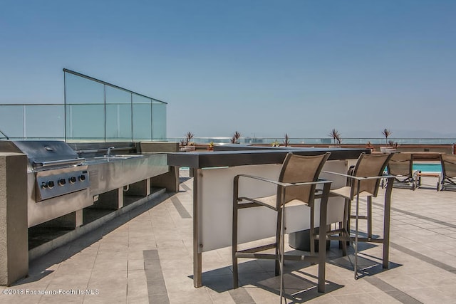 view of patio with a grill, an outdoor kitchen, an outdoor bar, and a water view